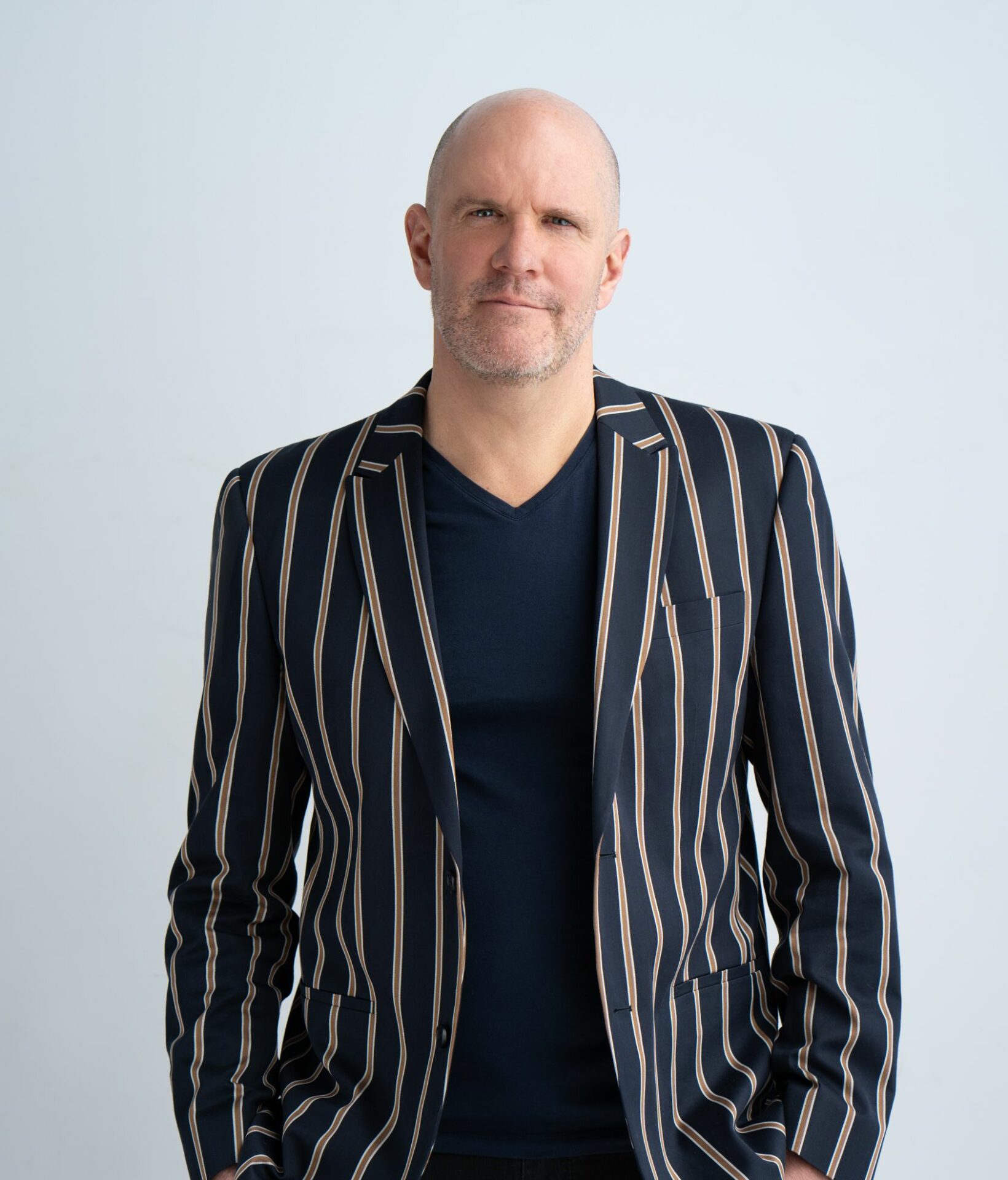 Patrice Croteau posing for headshot in a blue and grey striped suit jacket.